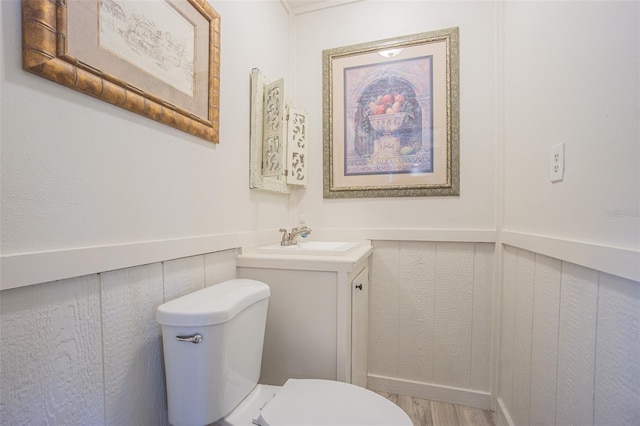 half bath with toilet, a wainscoted wall, wood finished floors, and vanity