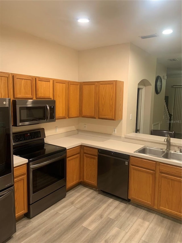 kitchen featuring appliances with stainless steel finishes, a sink, light wood-style floors, light countertops, and brown cabinets