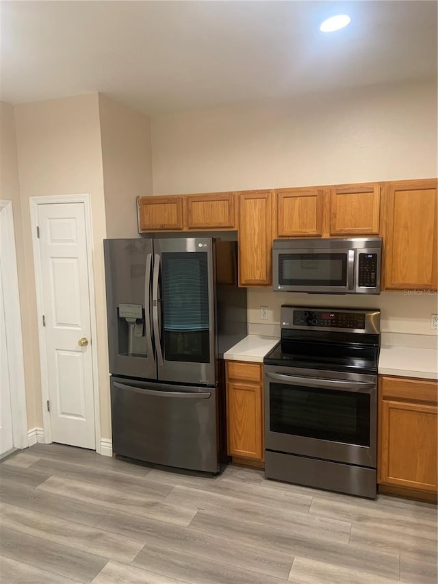 kitchen featuring stainless steel appliances, light countertops, brown cabinets, light wood finished floors, and recessed lighting