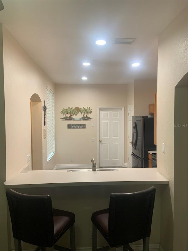 kitchen featuring freestanding refrigerator, a sink, recessed lighting, a breakfast bar, and a peninsula