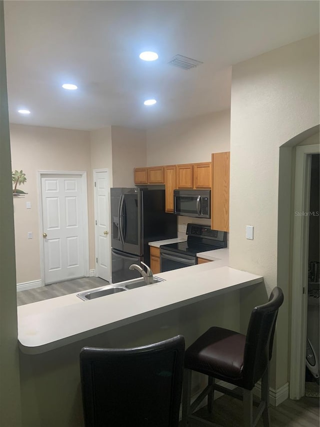kitchen featuring electric stove, a sink, refrigerator with ice dispenser, brown cabinetry, and a breakfast bar area