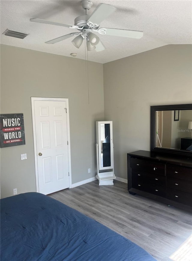 bedroom with wood finished floors, vaulted ceiling, a textured ceiling, ceiling fan, and baseboards