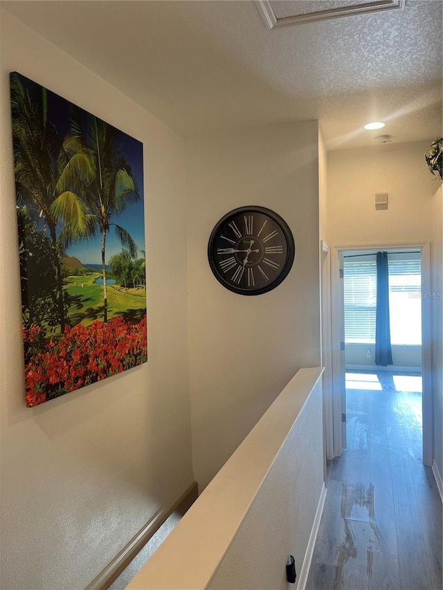 corridor with wood finished floors, a textured ceiling, and baseboards