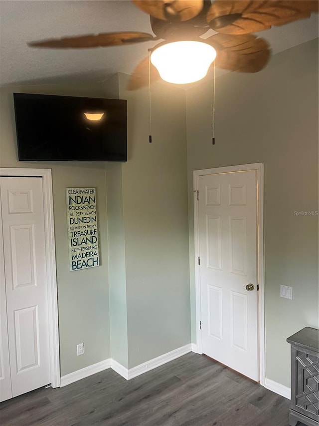 unfurnished bedroom featuring dark wood-type flooring, baseboards, a ceiling fan, and a wood stove