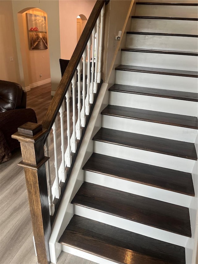 staircase with wood finished floors, arched walkways, and baseboards
