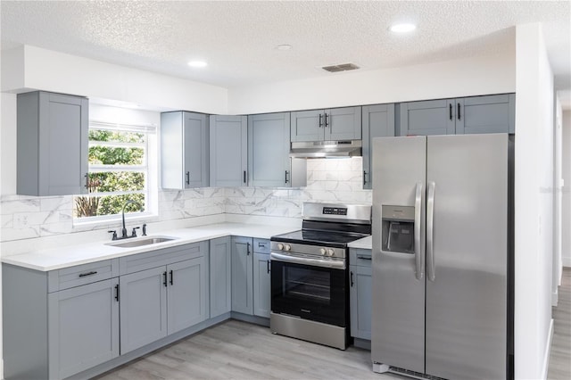 kitchen featuring appliances with stainless steel finishes, a sink, under cabinet range hood, a textured ceiling, and light countertops