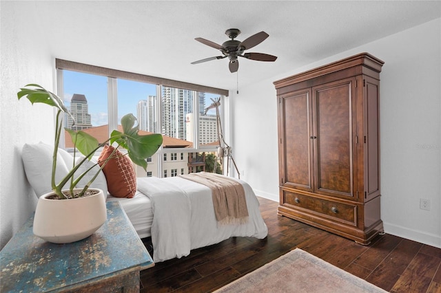 bedroom with dark wood-type flooring, a view of city, baseboards, and a ceiling fan