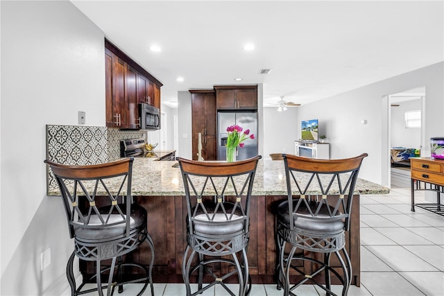 2270 Amherst Ave, Spring Hill, FL 34609 - kitchen with stainless steel appliances, a peninsula, a ceiling fan, light stone counters, and a kitchen breakfast bar