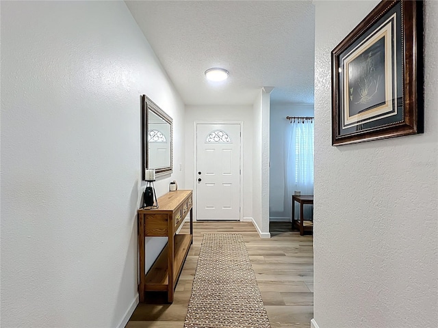 entryway with light wood-style floors, baseboards, a textured ceiling, and a textured wall