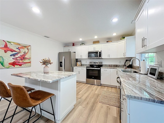kitchen featuring stainless steel appliances, a sink, ornamental molding, white cabinets, and a kitchen breakfast bar
