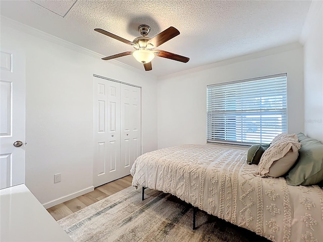bedroom featuring light wood finished floors, crown molding, a closet, a textured ceiling, and ceiling fan