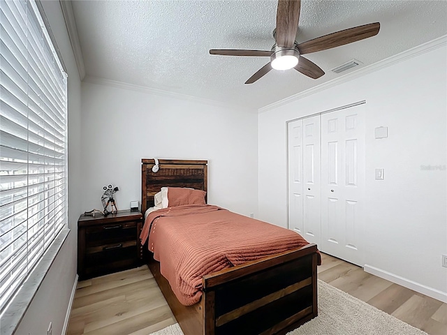 bedroom with light wood finished floors, ornamental molding, a textured ceiling, a ceiling fan, and a closet