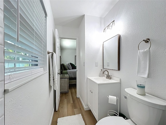 ensuite bathroom featuring wood finished floors, vanity, toilet, and a textured wall