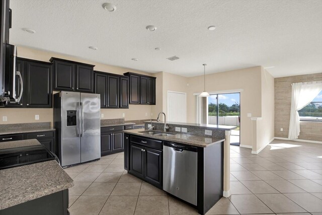 10106 Count Fleet Dr, Ruskin, FL 33575 - kitchen featuring stainless steel appliances, a sink, light tile patterned floors, dark cabinetry, and a kitchen island with sink
