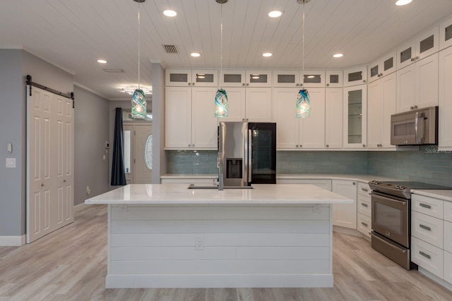 632 S Florida Ave, Tarpon Springs, FL 34689 - kitchen featuring appliances with stainless steel finishes, a barn door, an island with sink, backsplash, and light wood finished floors