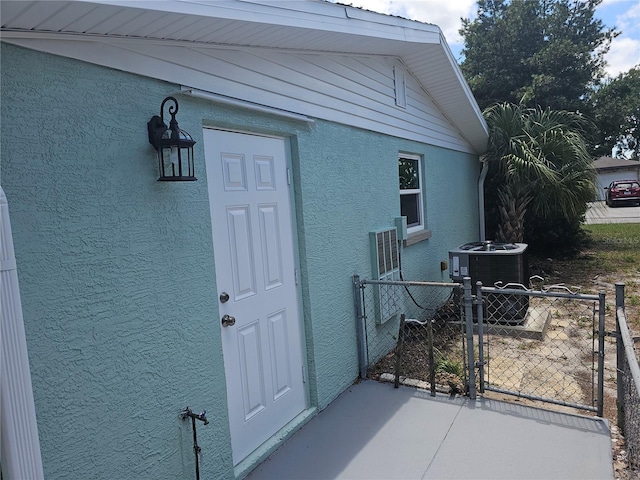 entrance to property featuring stucco siding, a gate, central AC, and fence