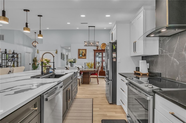 332 Wood Dove Ave, Tarpon Springs, FL 34689 - kitchen featuring stainless steel appliances, wall chimney exhaust hood, a sink, light wood-style flooring, and white cabinetry