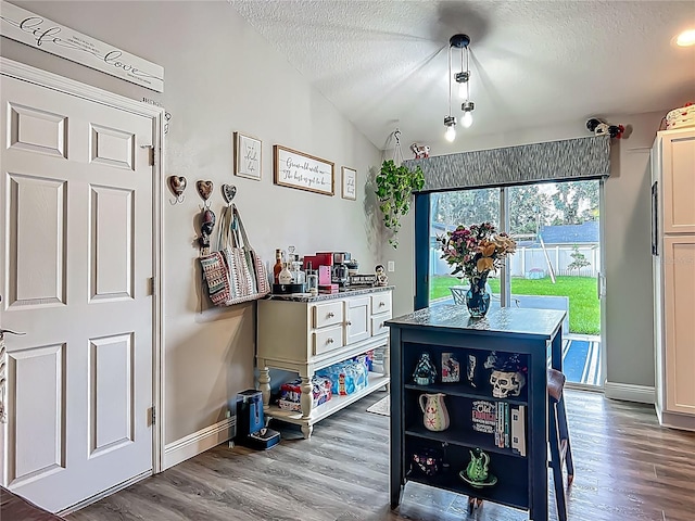 dining room featuring a textured ceiling, wood finished floors, baseboards, and lofted ceiling