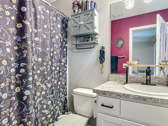 bathroom with a textured wall, toilet, vanity, and curtained shower