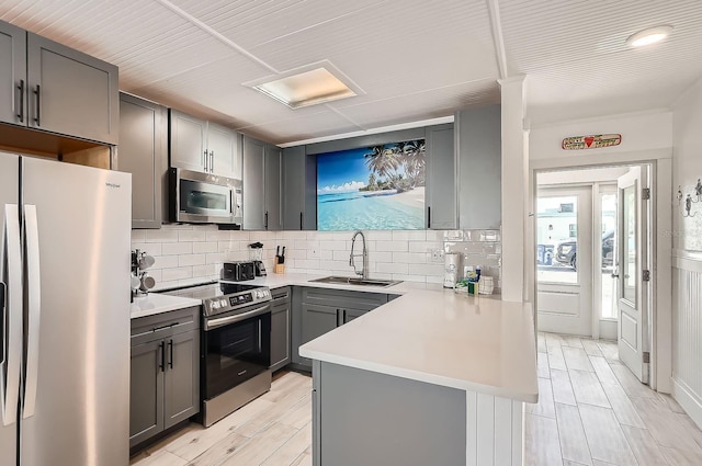 28 Seaside Ct, Holmes Beach, FL 34217 - kitchen with appliances with stainless steel finishes, a sink, gray cabinets, decorative backsplash, and a peninsula