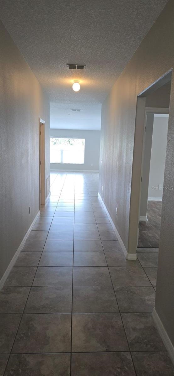 hallway featuring tile patterned floors, a textured ceiling, and baseboards