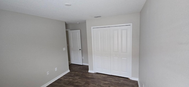 unfurnished bedroom with a closet, dark wood-type flooring, and baseboards