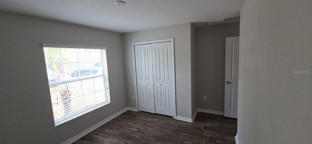 unfurnished bedroom with dark wood-type flooring, a closet, baseboards, and a textured ceiling