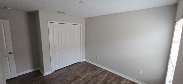 unfurnished bedroom with a closet, dark wood-style flooring, and baseboards