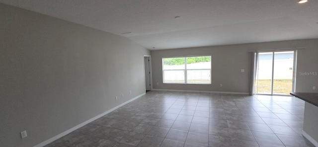 tiled spare room featuring lofted ceiling and baseboards