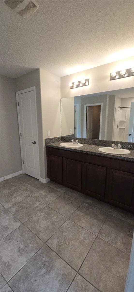 bathroom with double vanity, tile patterned flooring, baseboards, and a textured ceiling