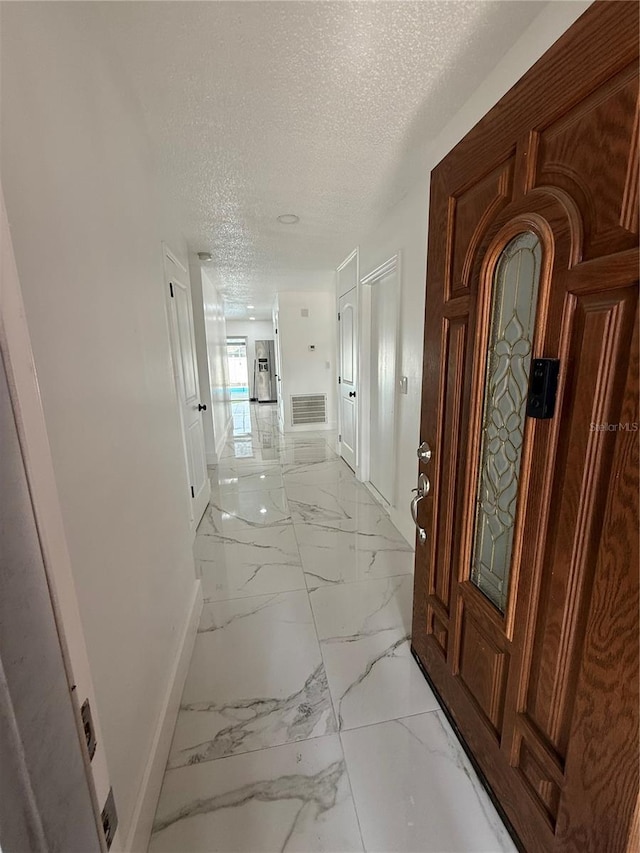 corridor featuring baseboards, light marble finish flooring, and a textured ceiling
