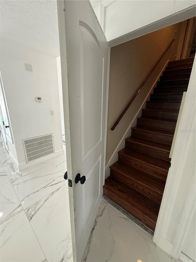 stairs with marble look tiles and a textured ceiling