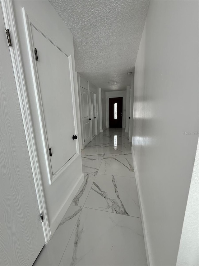 corridor with light marble finish flooring, a textured ceiling, and baseboards