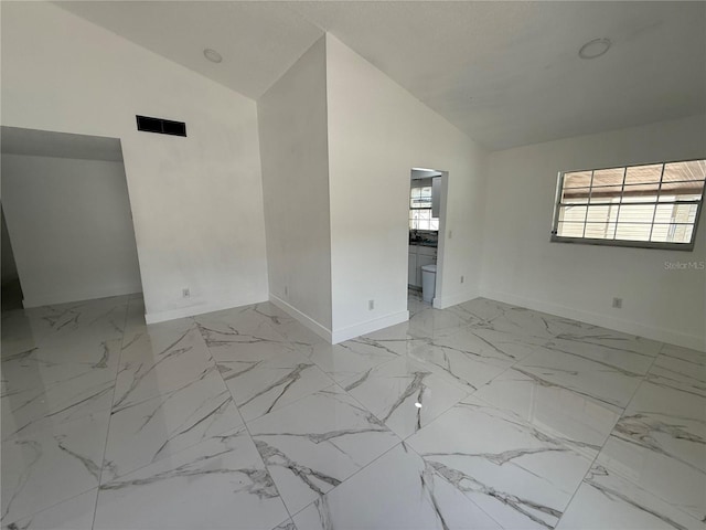spare room featuring lofted ceiling, baseboards, and light marble finish floors