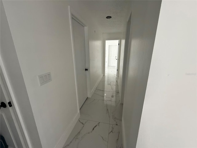 corridor featuring light marble finish flooring and baseboards