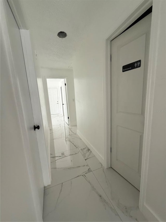 hallway with light marble finish flooring, baseboards, and a textured ceiling