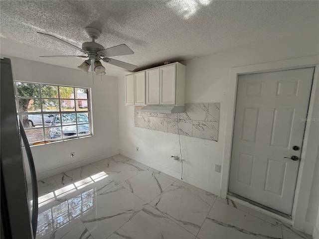 spare room with baseboards, light marble finish flooring, ceiling fan, and a textured ceiling