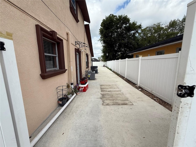 view of side of home with stucco siding, fence, cooling unit, and a patio