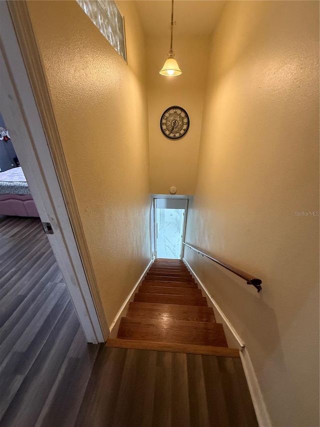 staircase with wood finished floors, baseboards, and a textured wall