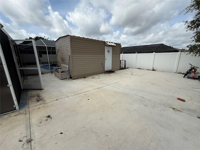 view of patio / terrace featuring a fenced backyard, an outbuilding, a storage shed, and a lanai