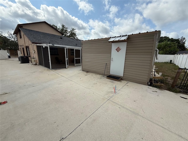 back of house featuring a sunroom, a patio area, fence, an outbuilding, and cooling unit