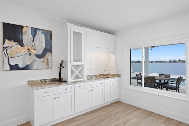 7060 S Shore Dr S, South Pasadena, FL 33707 - kitchen featuring light stone counters, white cabinets, light wood finished floors, a sink, and glass insert cabinets