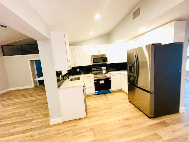 kitchen with appliances with stainless steel finishes, light wood-style flooring, white cabinetry, a sink, and vaulted ceiling