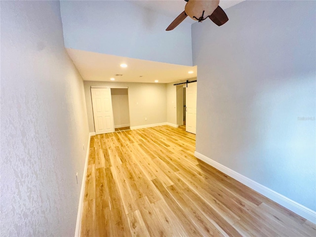 empty room featuring a ceiling fan, recessed lighting, light wood-type flooring, a high ceiling, and baseboards