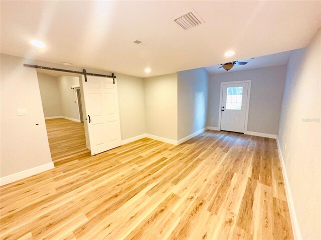 spare room with a barn door, light wood-type flooring, baseboards, and recessed lighting