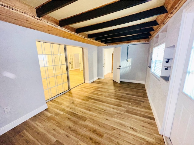 unfurnished bedroom featuring beam ceiling, wood finished floors, and baseboards