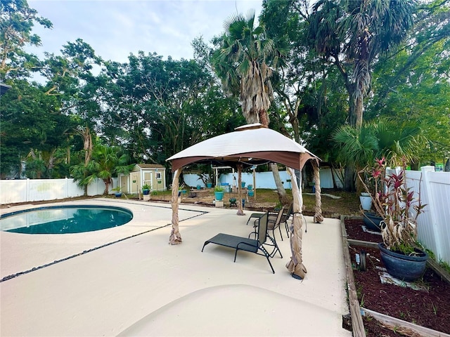 view of swimming pool featuring a gazebo, a fenced backyard, a patio, a shed, and an outdoor structure