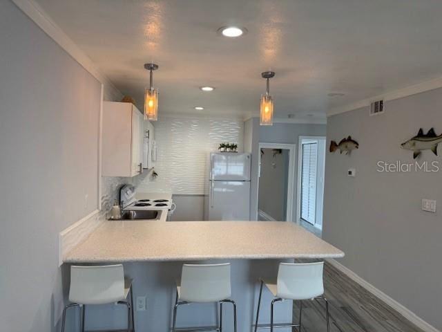 kitchen featuring white appliances, a peninsula, light countertops, a sink, and white cabinets