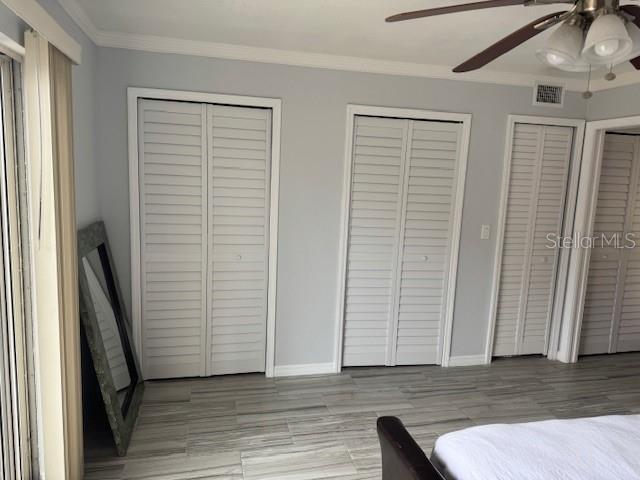 bedroom with two closets, crown molding, baseboards, and a ceiling fan