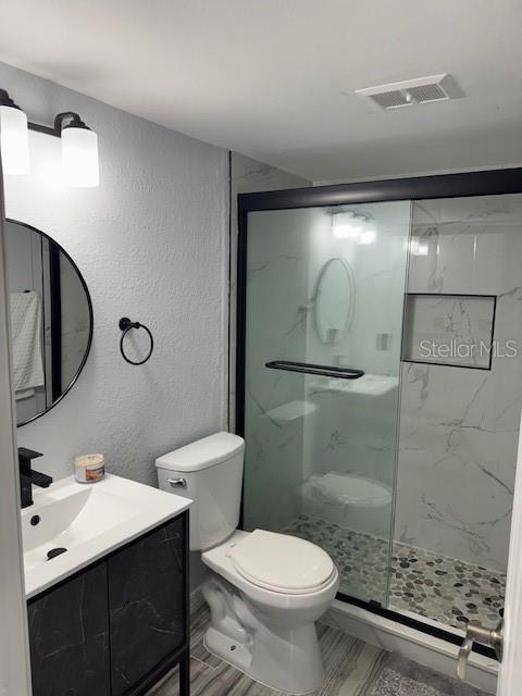 full bathroom featuring a shower stall, toilet, a textured wall, and vanity
